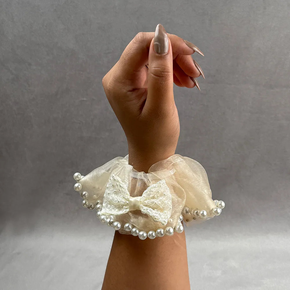 Hand wearing a decorative beige lace scrunchie with pearls on a gray background