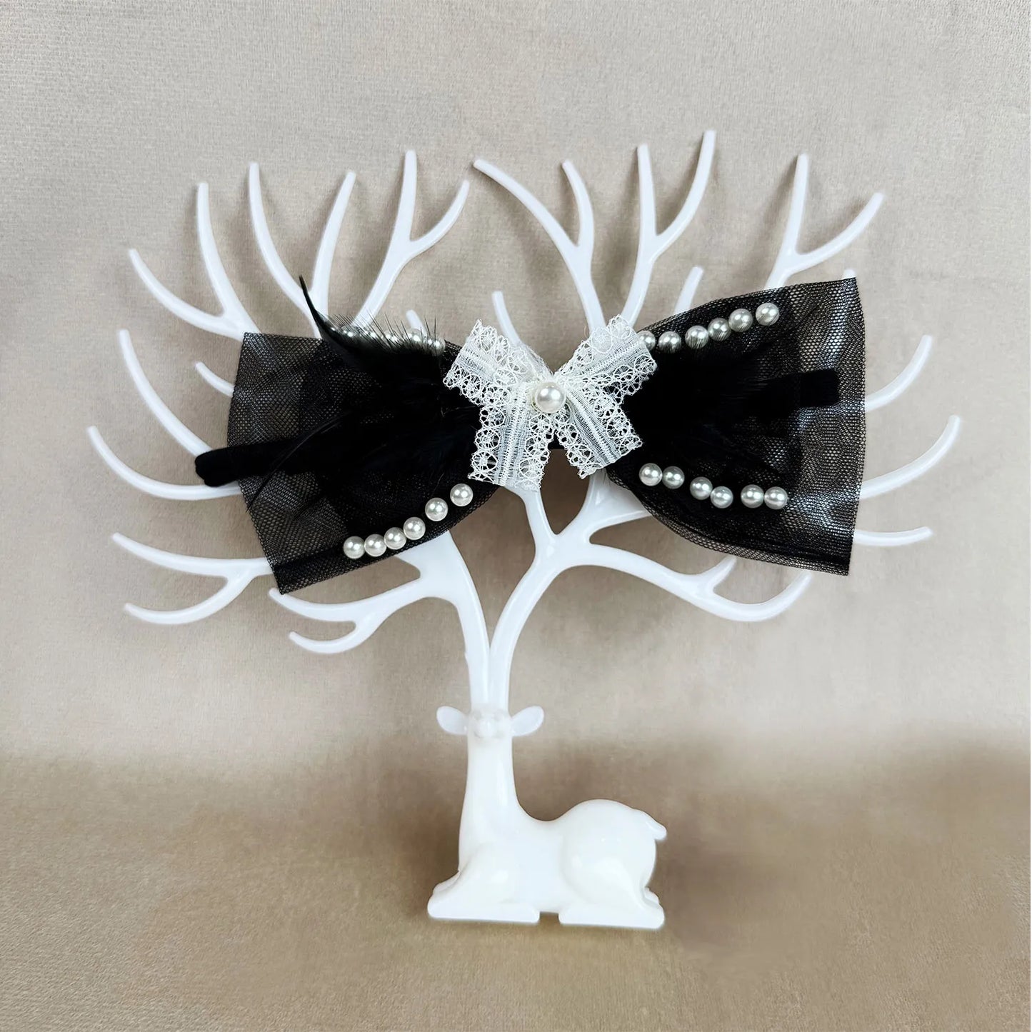 Black bow headband with white lace and pearls on a white tree-shaped stand against a beige background