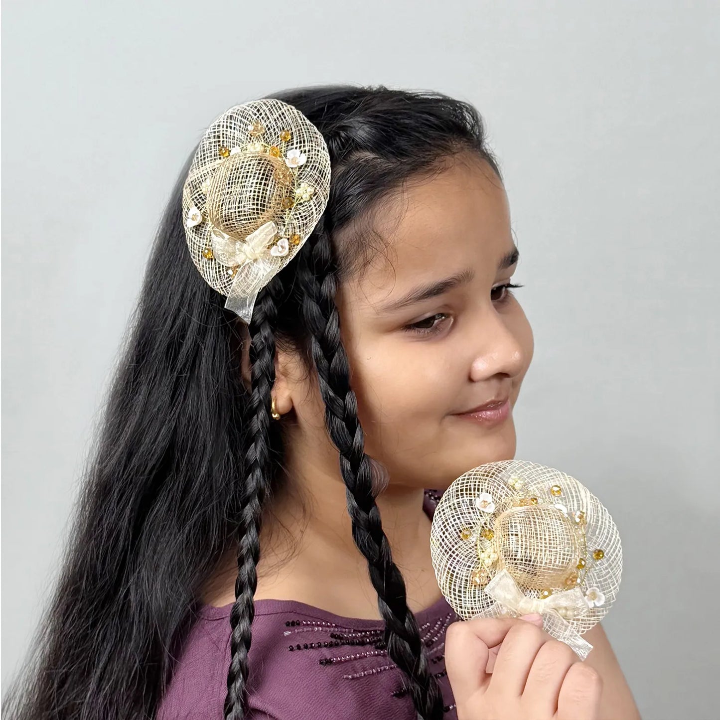 Girl wearing golden fascinator hair clip with floral embellishments with similar piece in hand