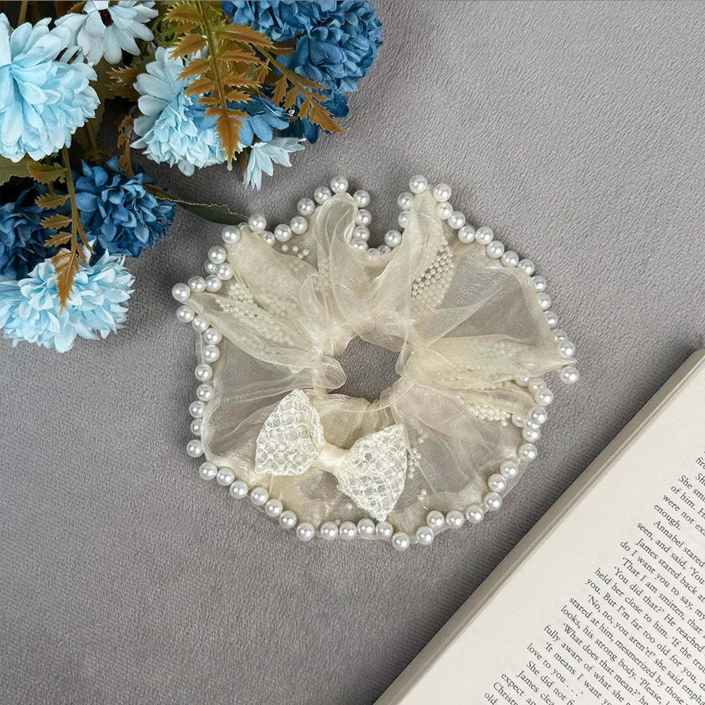 Decorative scrunchie with pearls on a gray surface with flowers and a book.