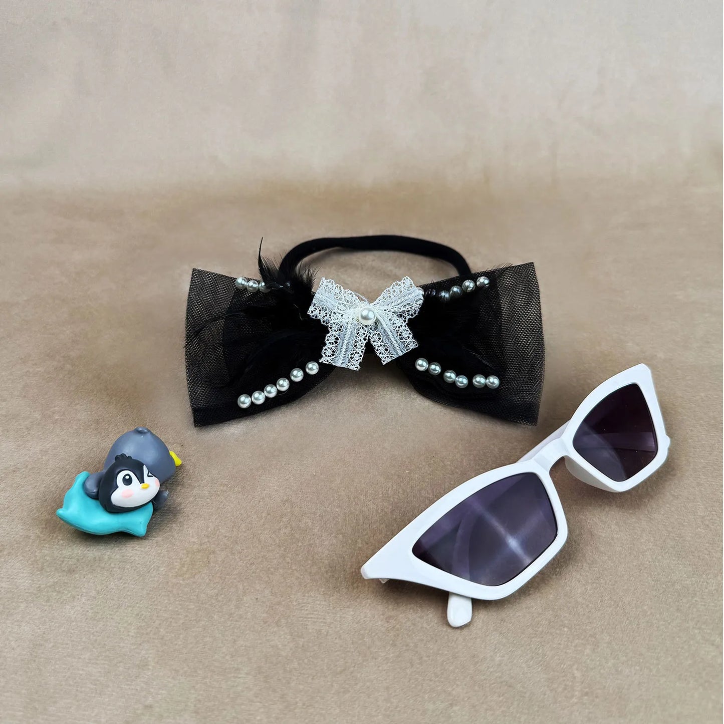 Black bow headbands with pearls, white sunglasses, and small penguin figurine on a beige background