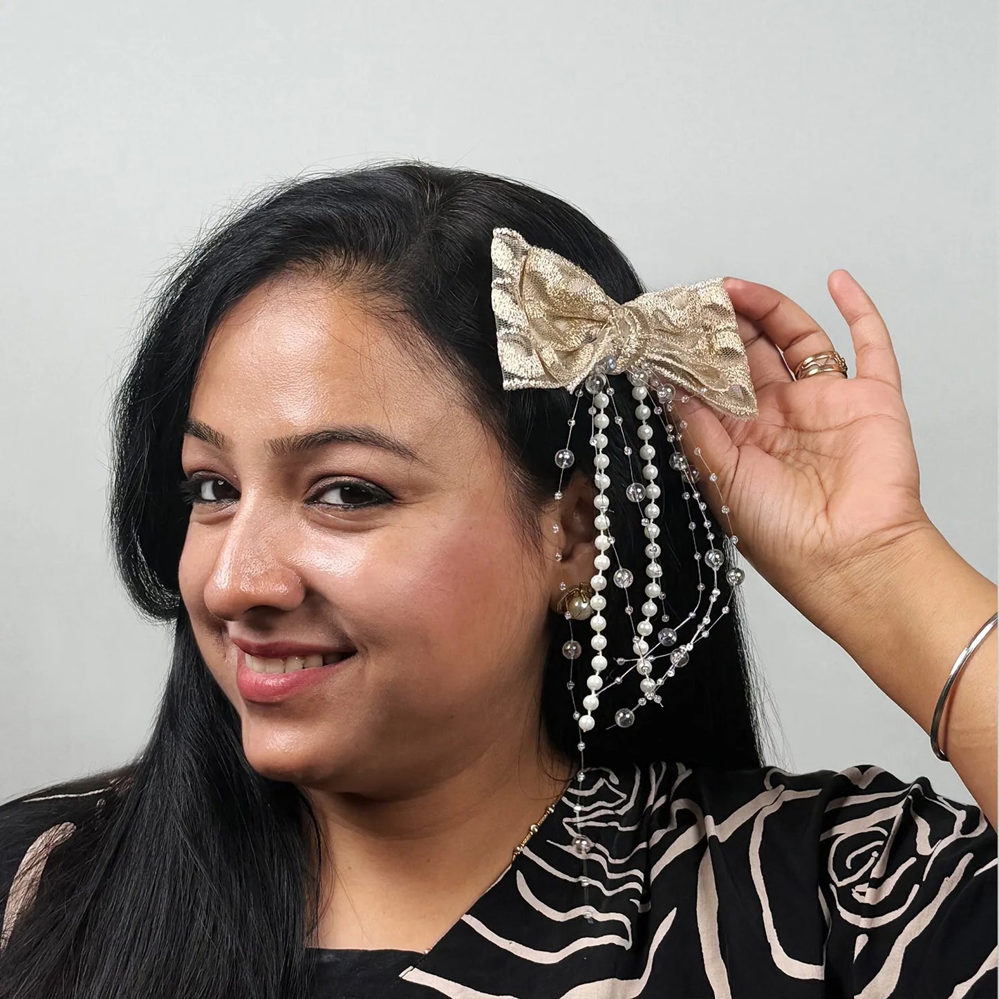 Woman holding a decorative hair accessory with a bow and beads against a plain background