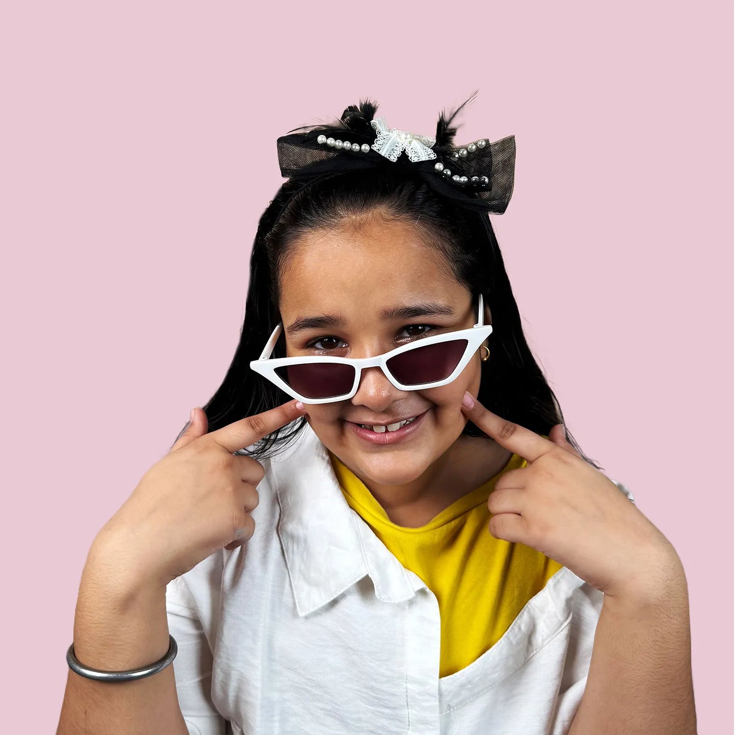 Young girl wearing black headband and sunglasses on a pink background