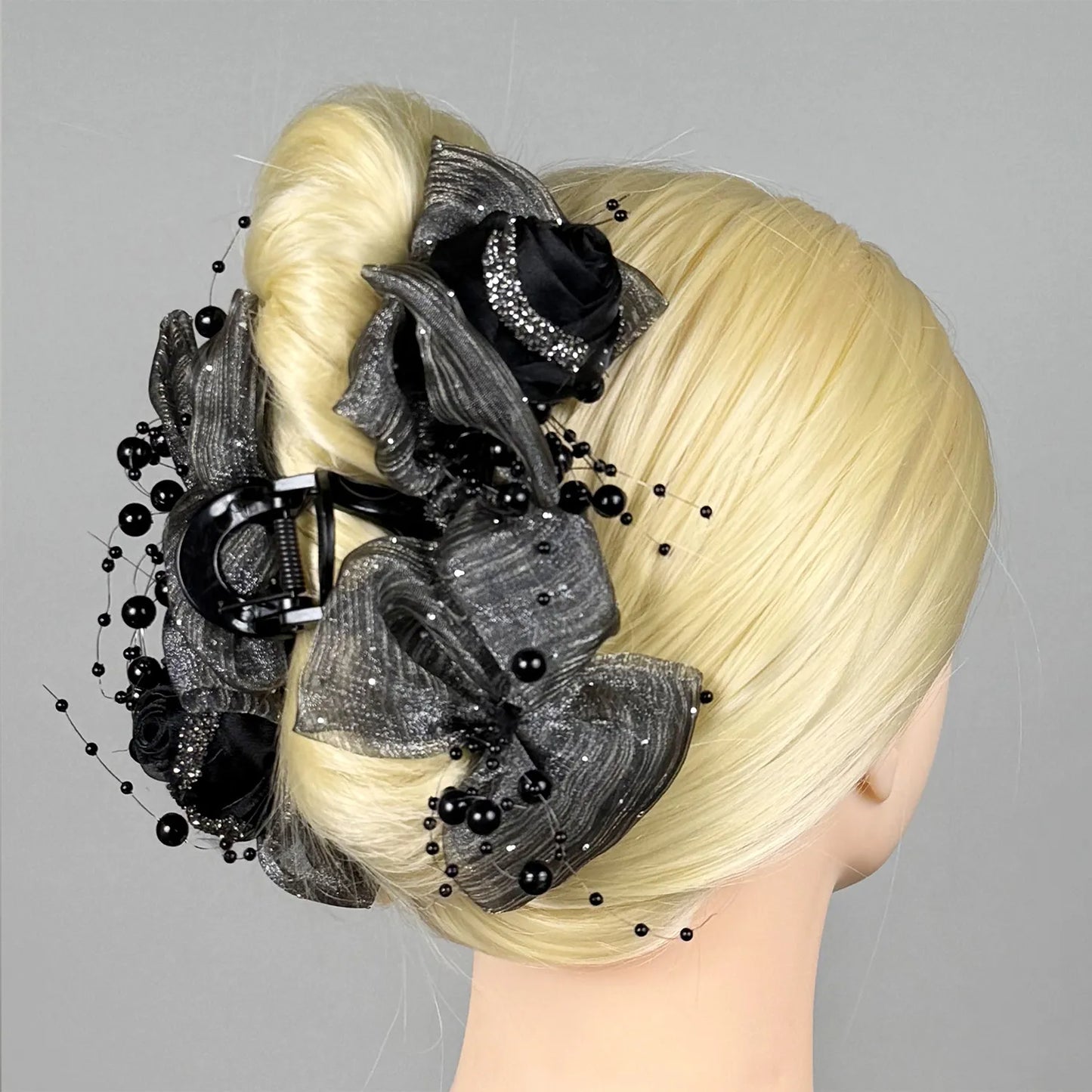 Blonde hair styled in an intricate updo with grey floral hair claw and beads on a gray background