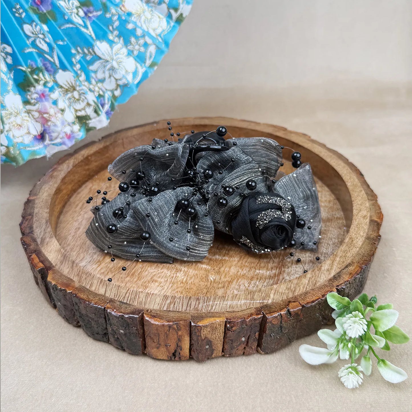 Grey decorative flower hair clutcher on a wooden slice with a floral background