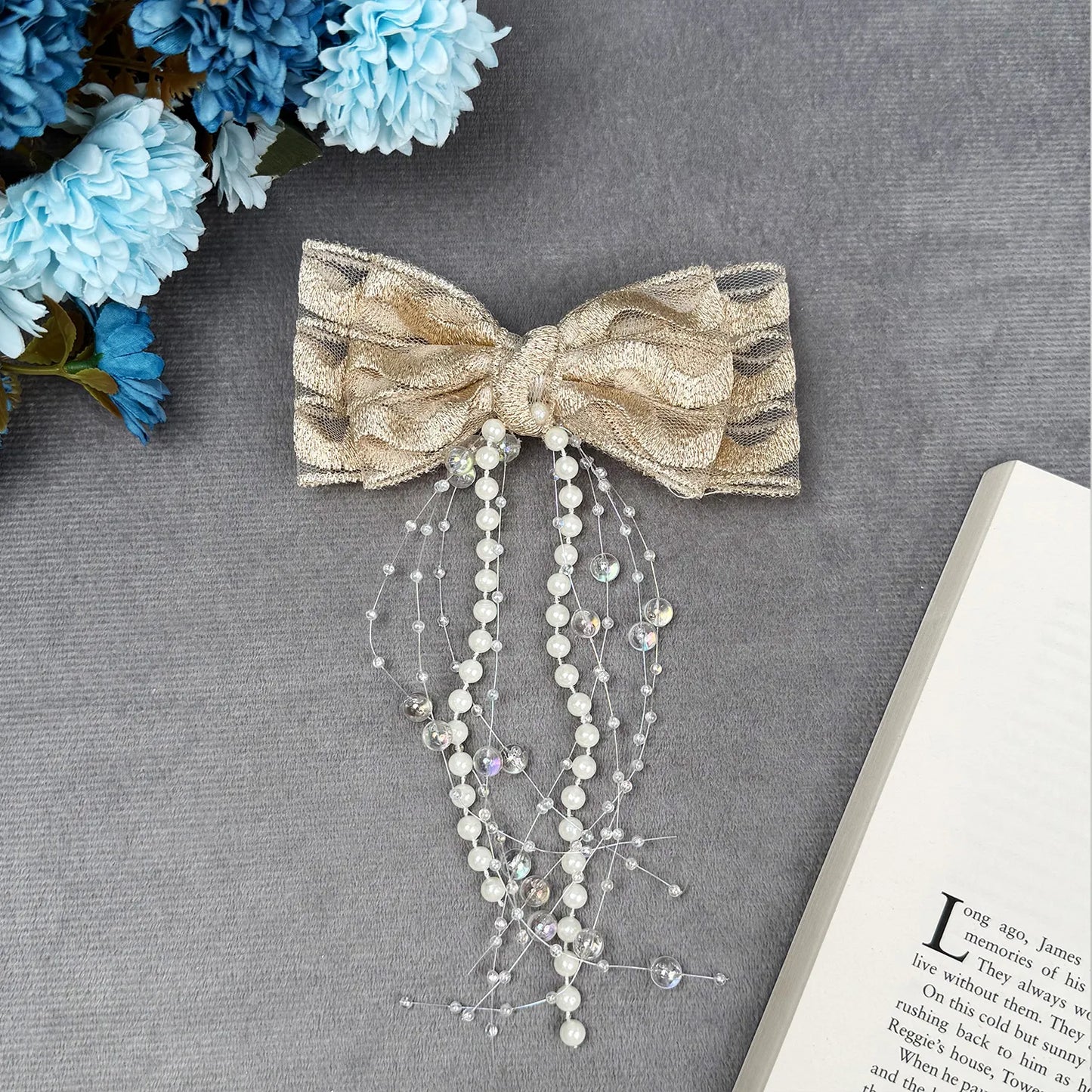 Decorative bow with beads on a gray surface with blue flowers and an open book.