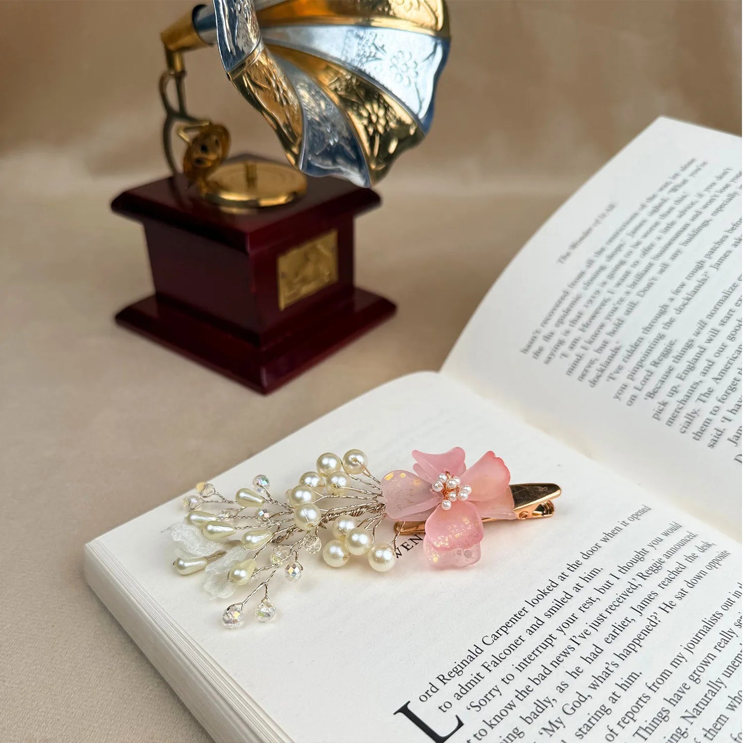 Decorative hair clip with pink flower and pearls on an open book with a vintage gramophone in the background.