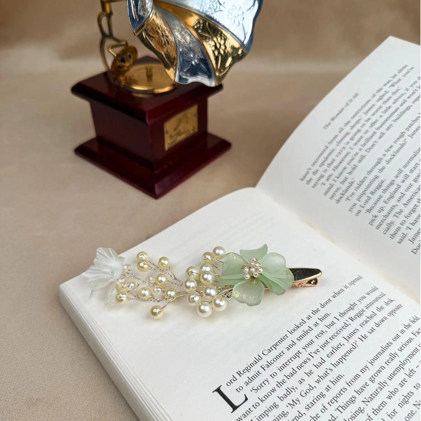 Decorative hair clip with green flower and pearls on an open book with a vintage gramophone in the background.