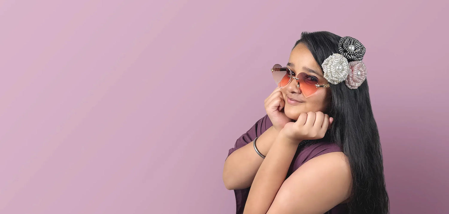 Young girl with decorative hair clips and sunglasses posing against a pink background