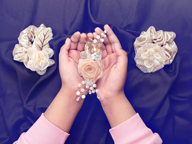 Decorative hair accessories with flowers and pearls held in hands against a purple fabric background