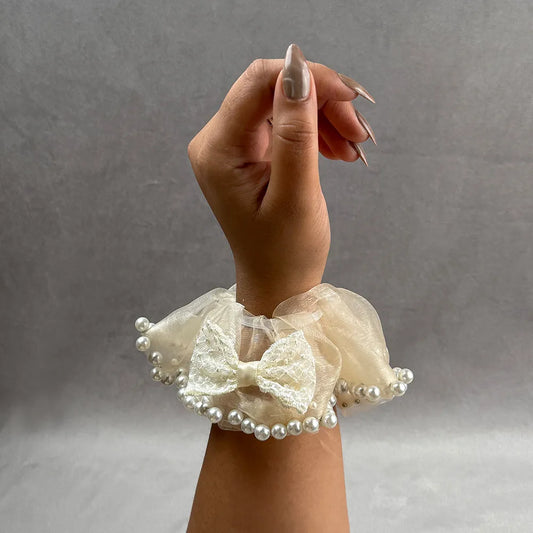 Hand wearing a decorative beige lace scrunchie with pearls on a gray background