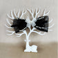 Black bow headband with white lace and pearls on a white tree-shaped stand against a beige background