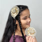 Girl wearing golden fascinator hair clip with floral embellishments with similar piece in hand