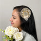Women wearing golden fascinator hair clip with floral embellishments and flowers in hand
