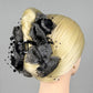 Blonde hair styled in an intricate updo with grey floral hair claw and beads on a gray background