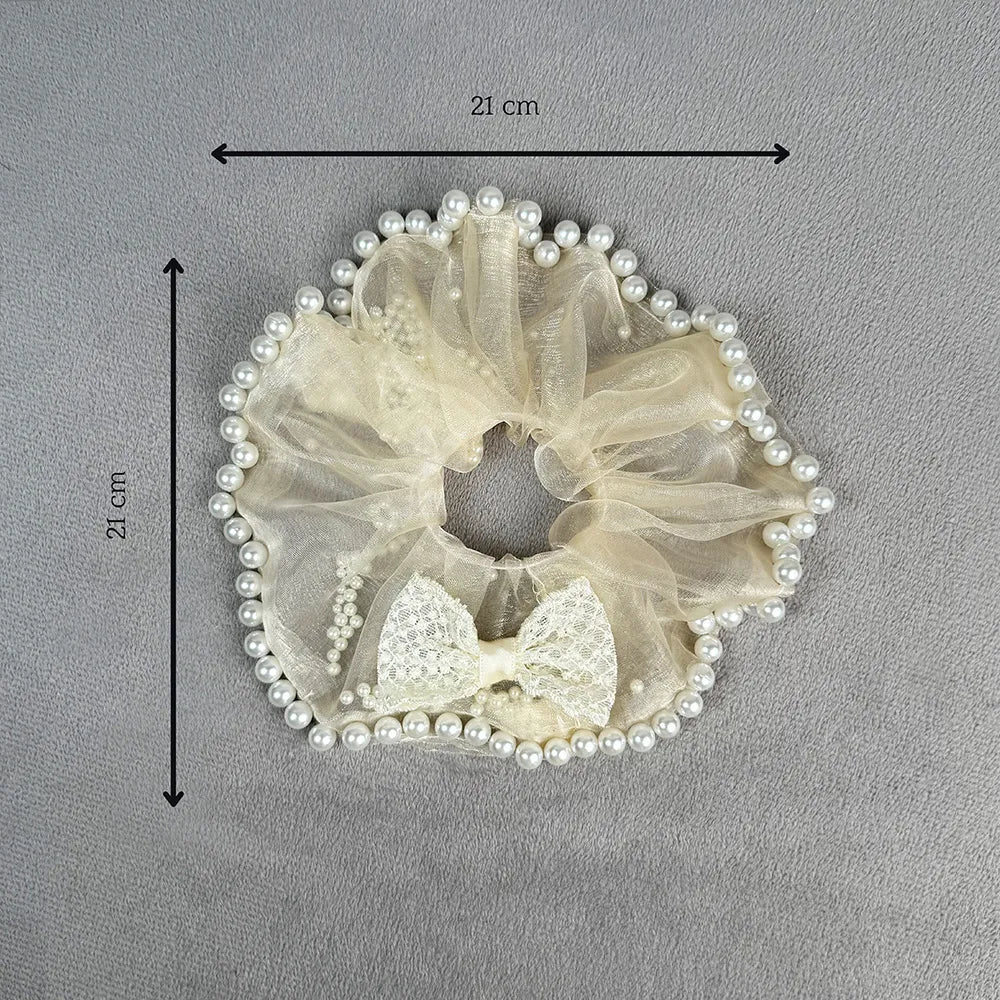 Off white scrunchie with bow and pearls on a gray background, shown with measurements.