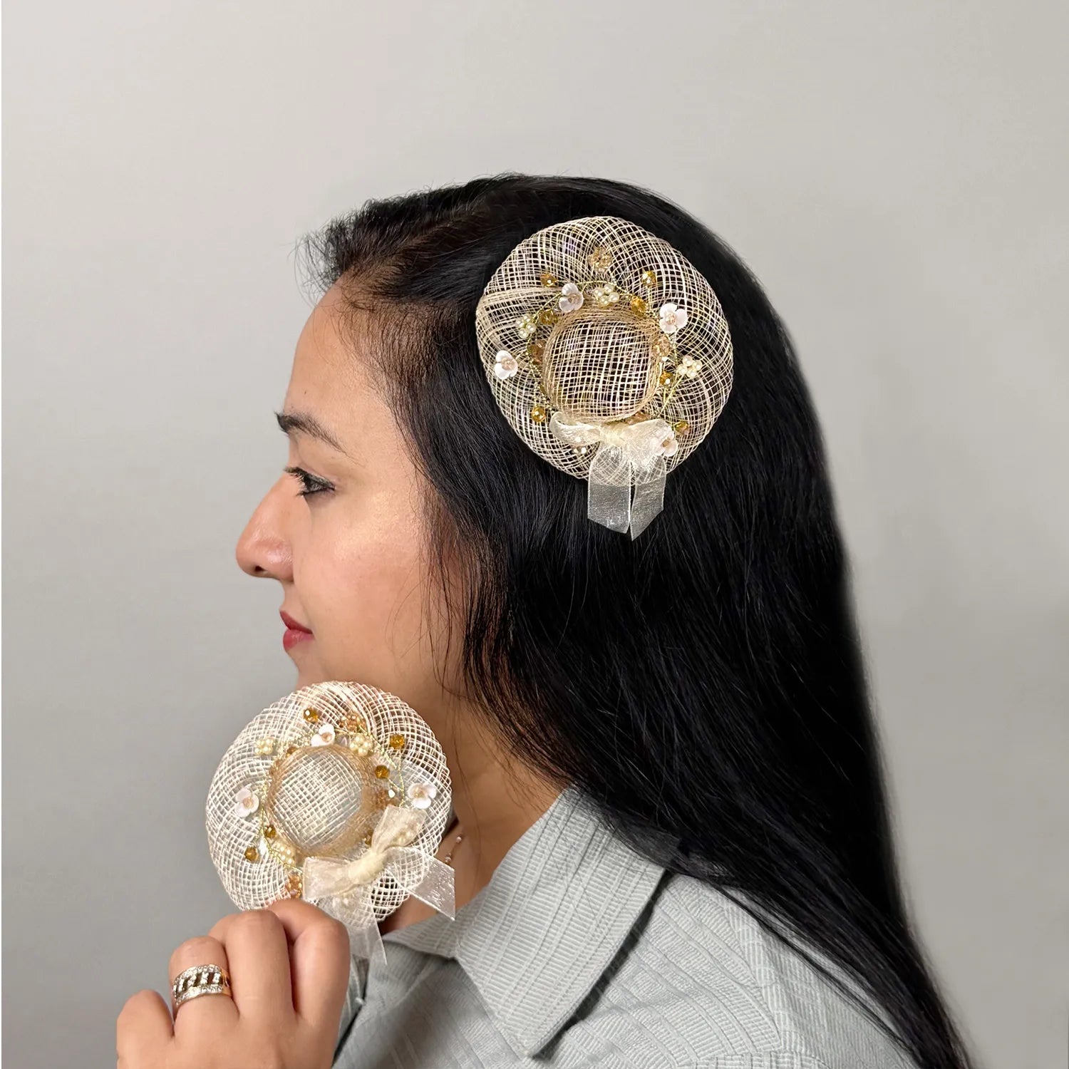 Women  wearing golden fascinator hair clip with floral embellishments with similar piece in hand