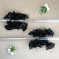 Black floral hair claw clips on a beige background with decorative elements.