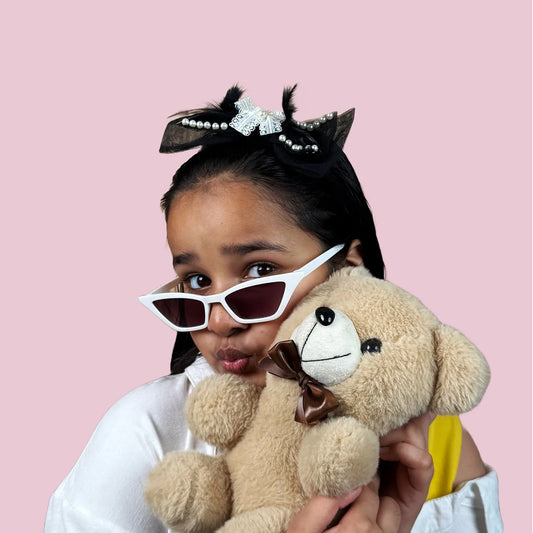 Child wearing designer black headband holding a teddy bear against a pink background
