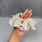Hand holding a decorative bow scrunchie with pearls against a gray background