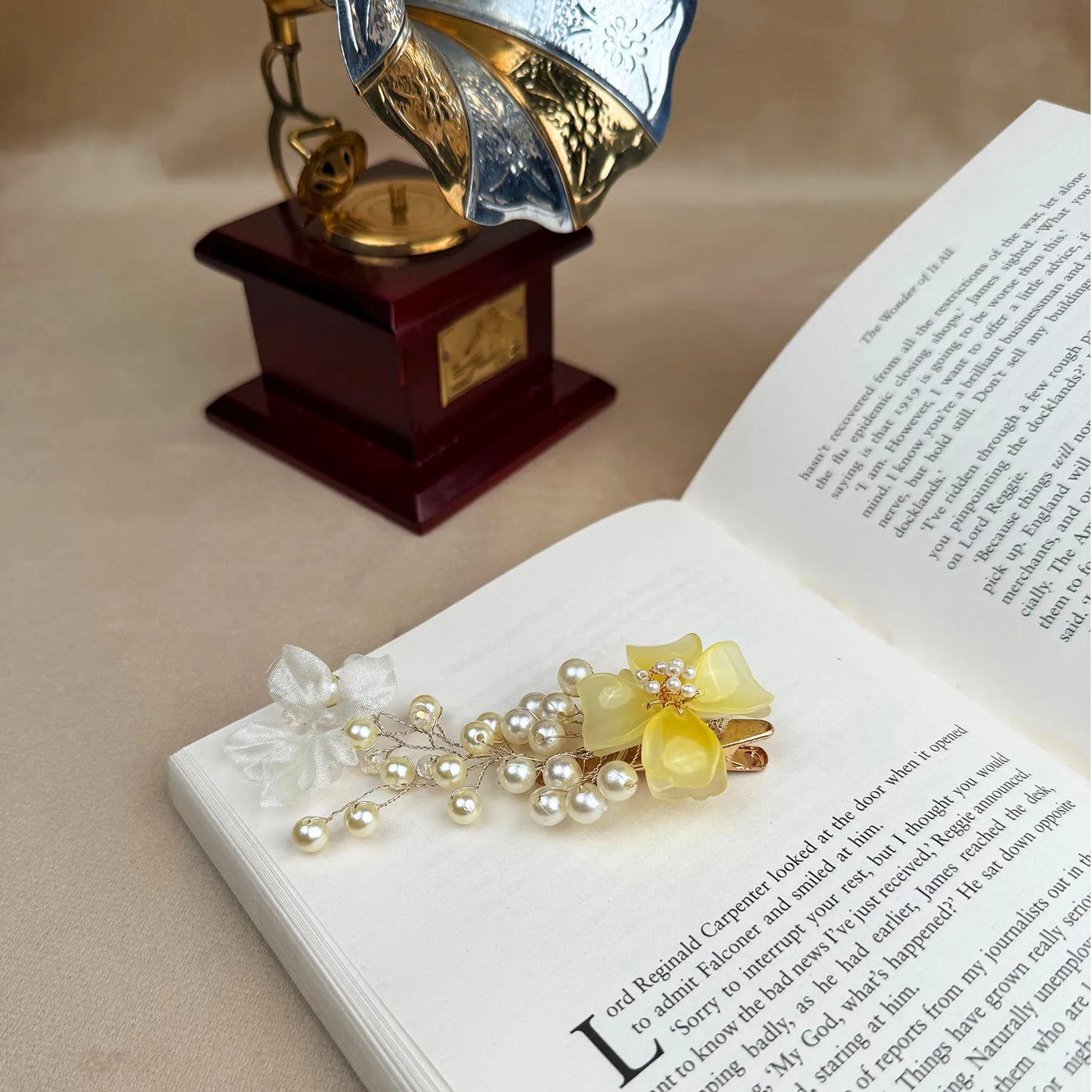 Decorative hair clip with yellow flower and pearls on an open book with a vintage gramophone in the background.