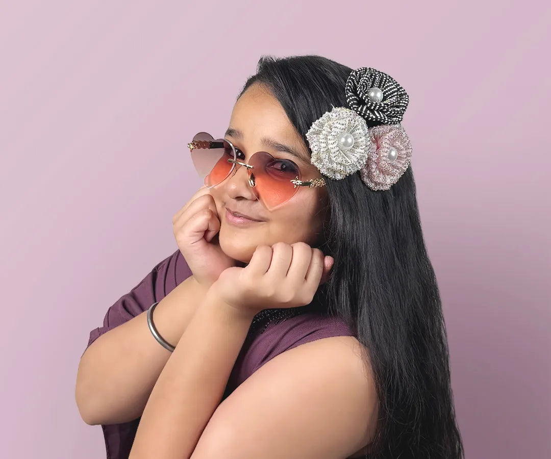 Woman wearing heart-shaped sunglasses and decorative hair accessories against a pink background